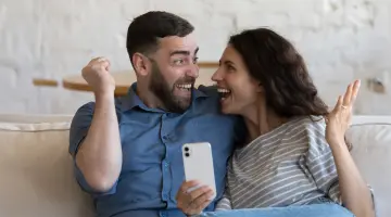 Lachendes Pärchen auf der Couch mit Handy.