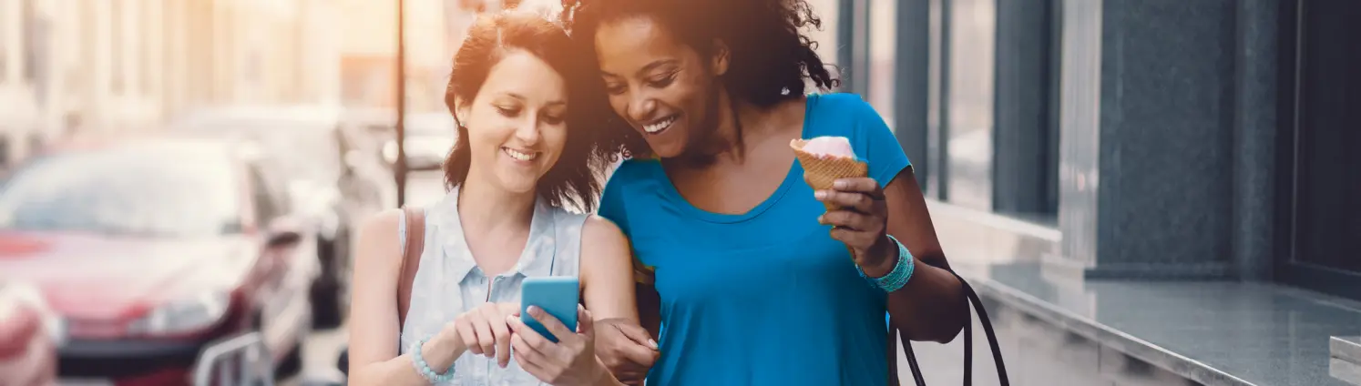 Zwei Frauen laufen auf einer Staße und schauen gemeinsam auf ein Handy