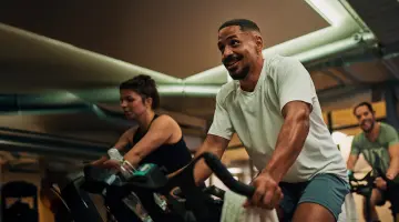 Junger sportlicher Mann sitzt auf einem Fahrrad im Fitnessstudio