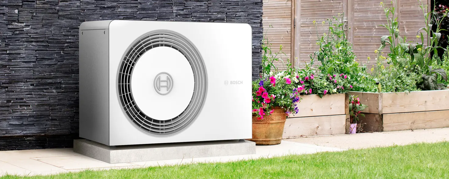 Eine Wärmepumpe steht im Garten neben Pflannzenkübeln