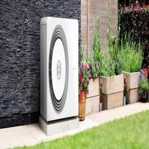 Eine Wärmepumpe steht im Garten neben Pflannzenkübeln