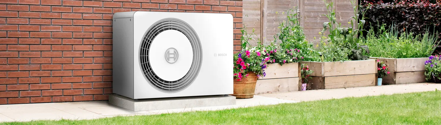Eine Wärmepumpe steht im Garten neben Pflannzenkübeln