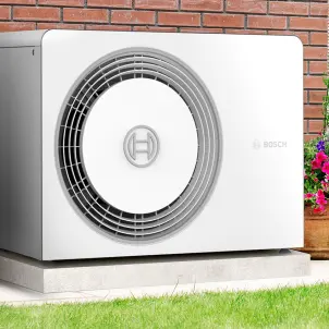 Eine Wärmepumpe steht im Garten neben Pflannzenkübeln