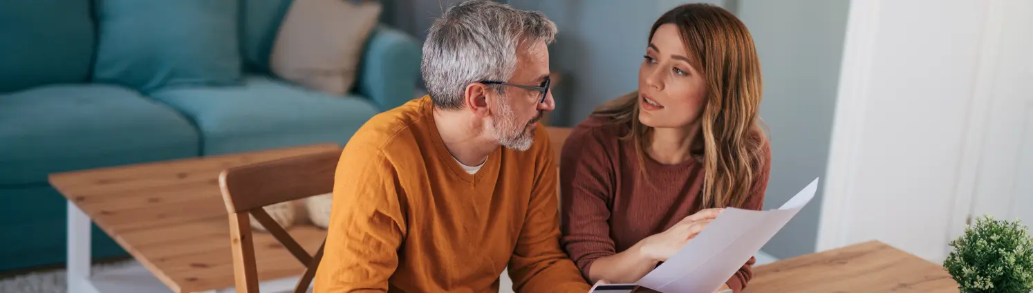 Eine Frau und ein Mann sitzen an einem Tisch und besprechen sich vor einen Laptop und Papieren