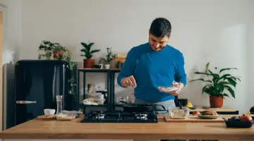 Mann mit blauem Pullover kocht in der Küche