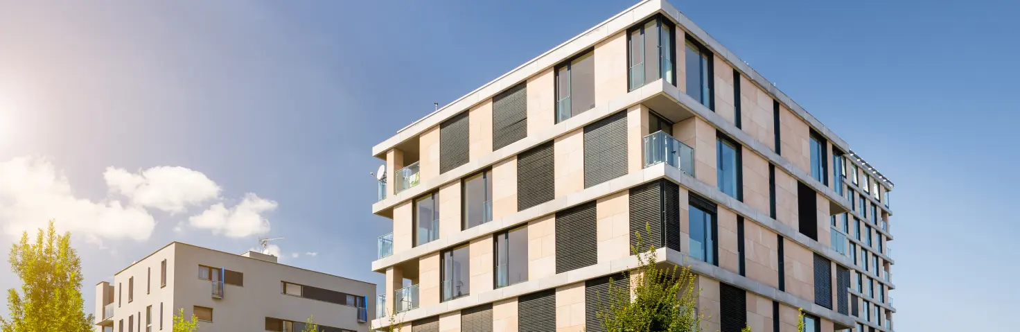 Ein modernes Mehrfamilienhaus vor blauem Himmel mit grünen Bäumen vor dem Gebäude