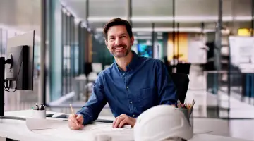 Mann sitzt in einem Architektenbüro am Schreibtisch und macht Skizzen mit einem Stift