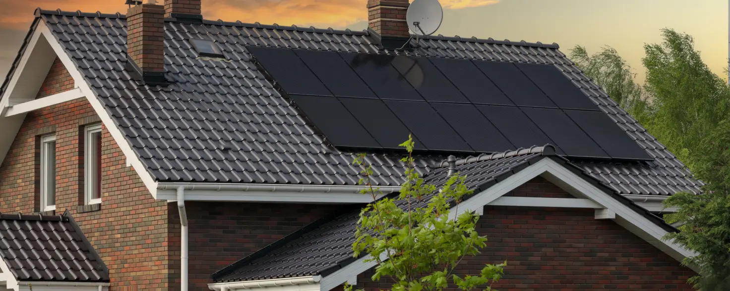 Einfamilienhaus mit Photovoltaikanlage vor rötlichem Abendhimmel.