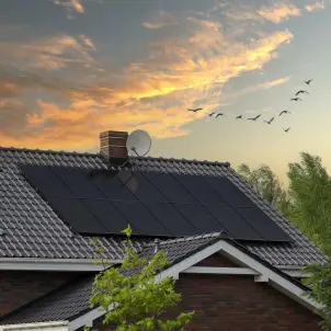 Einfamilienhaus mit Photovoltaikanlage vor rötlichem Abendhimmel.