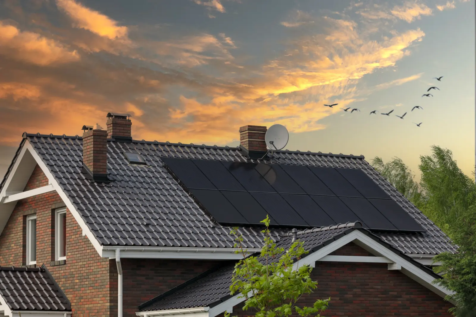 Einfamilienhaus mit Photovoltaikanlage vor rötlichem Abendhimmel.