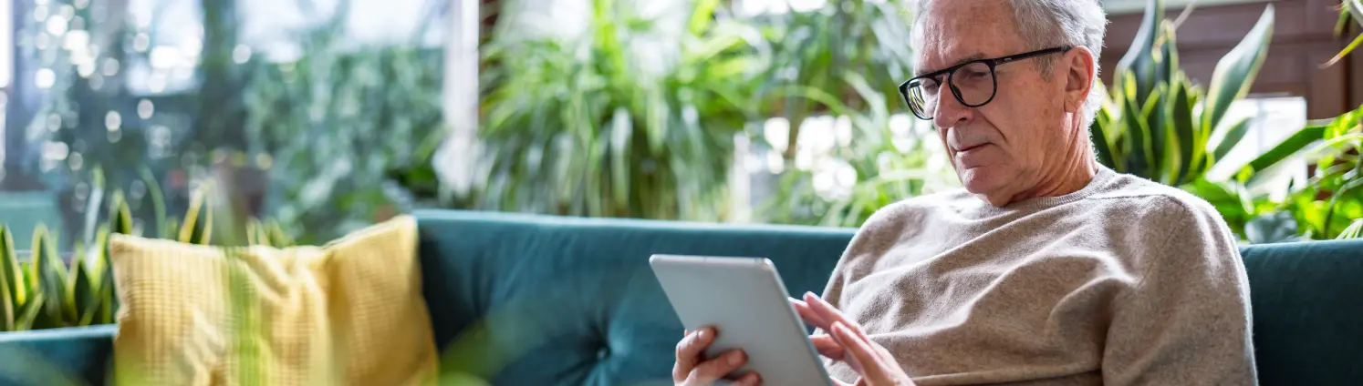 Älterer Mann mit digitalem Tablet, während er zu Hause auf dem Sofa im Wohnzimmer sitzt
