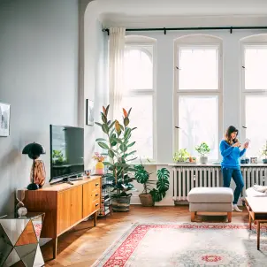 eine Frau steht in ihrem Wohnzimmer und schaut auf ihr Telefon
