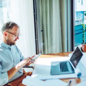 Mann mit Smartphone, Laptop und Solar-Paneel am Schreibtisch.
