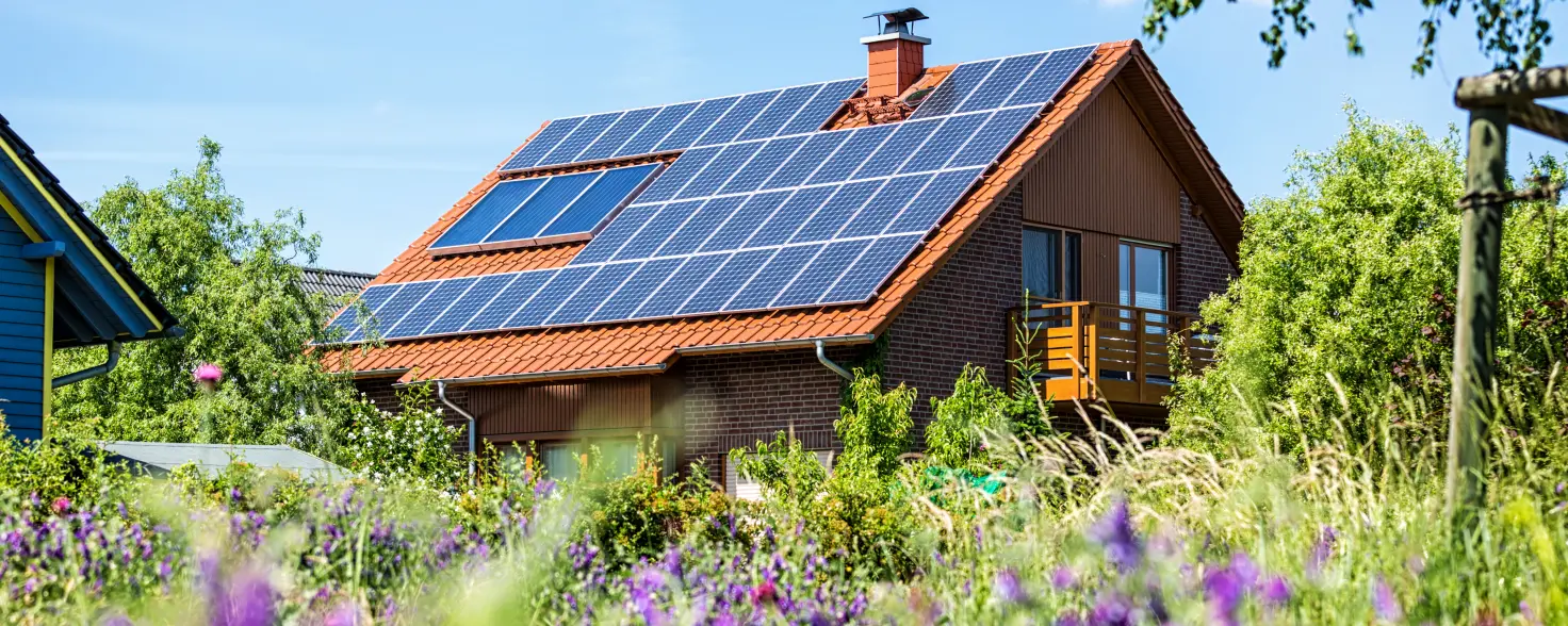 Haus mit PV-Anlage auf dem Dach im Sommer und im Vordergrund sind Blumen