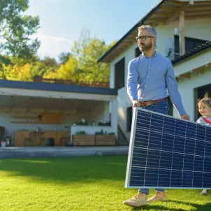 Vater und Tochter tragen ein Solarmodul vor dem Haus