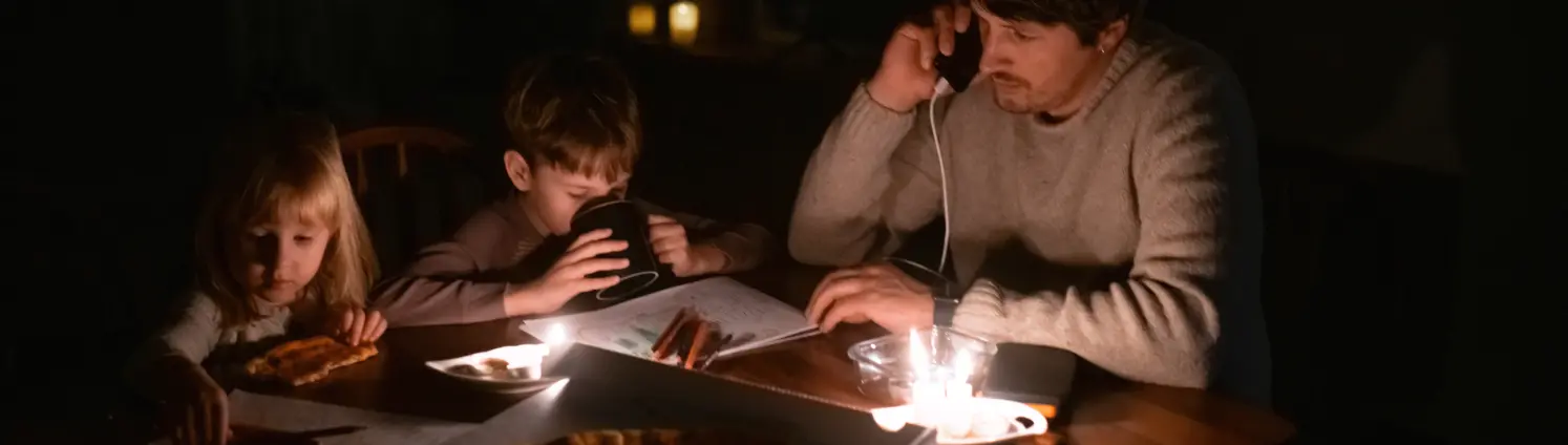 Familie sitzt zu Hause mit Kerzen und isst Pizza während eines Stromausfalls.