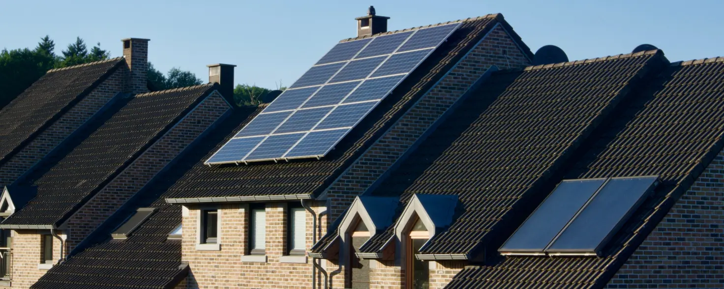 Solaranlage auf dem Dach eines Klinkerhauses an einem sonnigen Tag mit Bäumen im Hintergrund.
