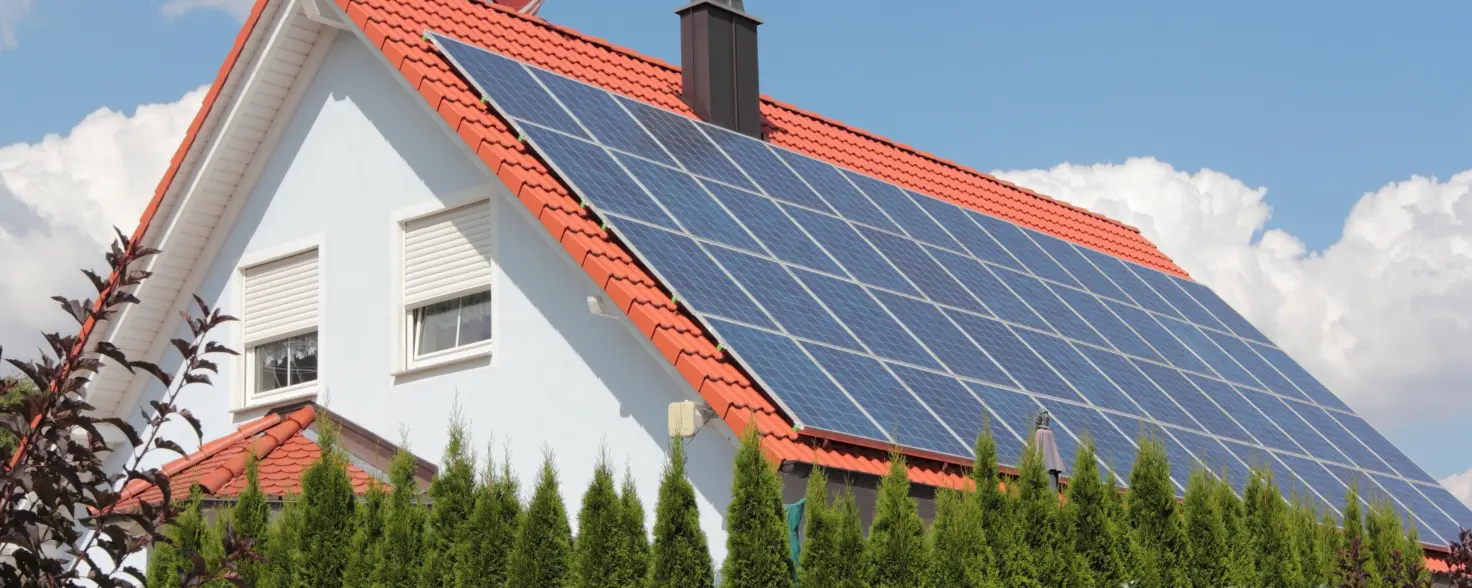 Eigenheim hinter einer Hecke mit einer Solaranlage auf dem Dach.