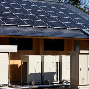 Satteldach mit Photovoltaik-Paneelen und darunter aufgereihten Stromspeicherkästen.