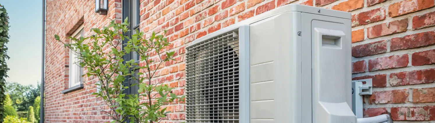 Seitenansicht der Wärmepumpe im Freien, die an einem sonnigen Tag an der Ziegelmauer des schönen Hauses hängt.