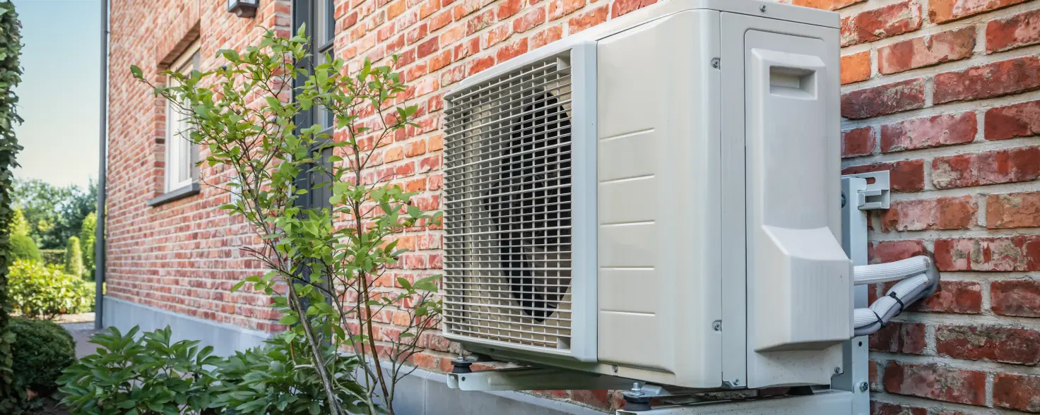 Seitenansicht der Wärmepumpe im Freien, die an einem sonnigen Tag an der Ziegelmauer des schönen Hauses hängt.
