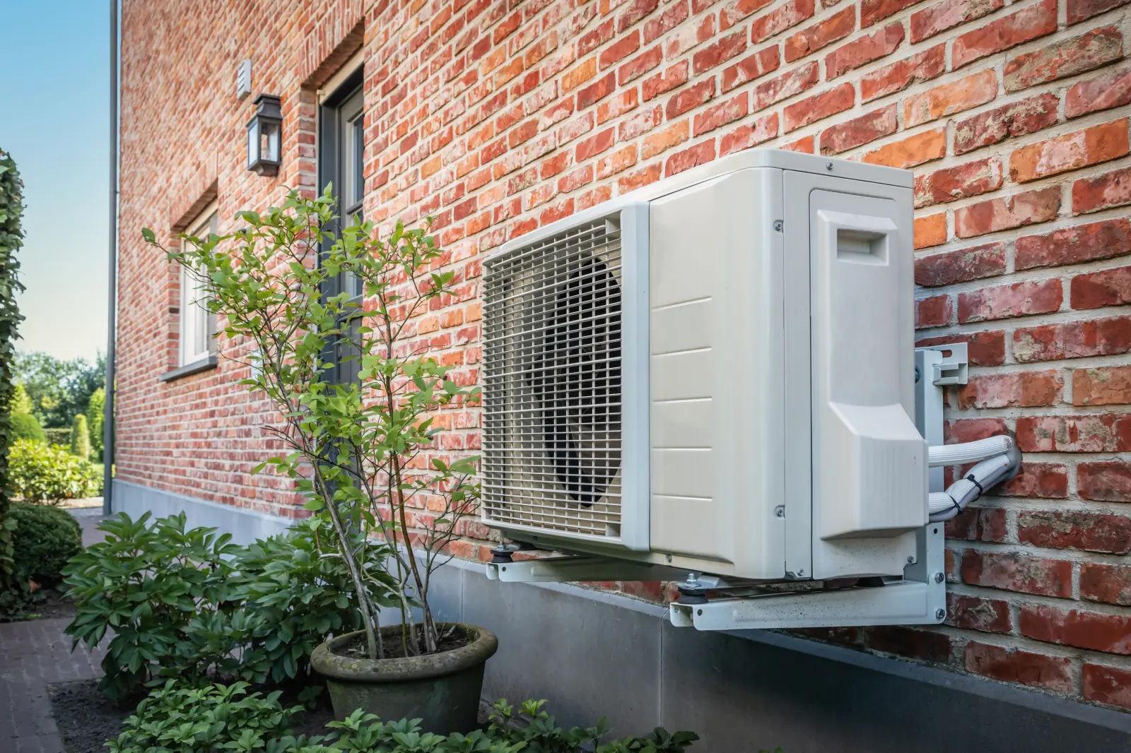 Seitenansicht der Wärmepumpe im Freien, die an einem sonnigen Tag an der Ziegelmauer des schönen Hauses hängt.