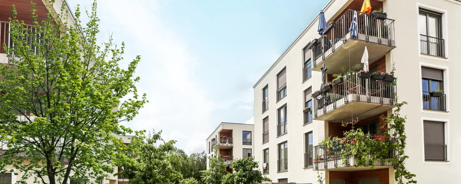 Ein modernes Mehrfamilienhaus mit Balkonen vor blauem Himmel mit grünen Bäumen im Vordergrund
