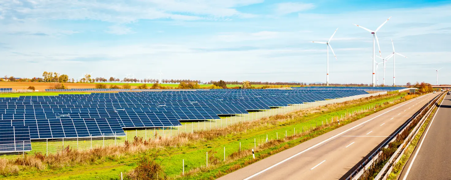 Auf einem Feld neben einer Straße ist eine Photovoltaik-Anlage und Windkrafträder zu sehen Bild mit KI erstellt.