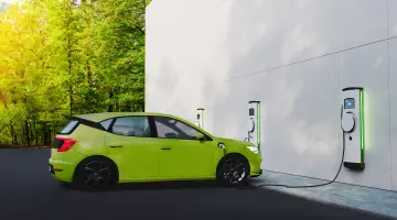Ein grünes E-Auto lädt an einer Wallbox, die an einer Wand montiert ist