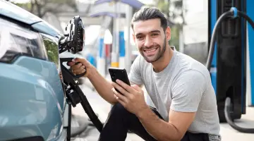 Ladestation: Junger Mann, der sein Elektroauto mit einem Typ-2-Stecker lädt.
