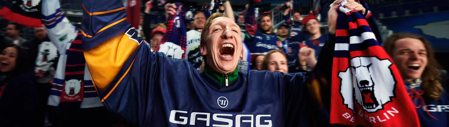 Ein Eisbären-Fan jubelt in einem Fantrikot mit GASAG-Aufschrift