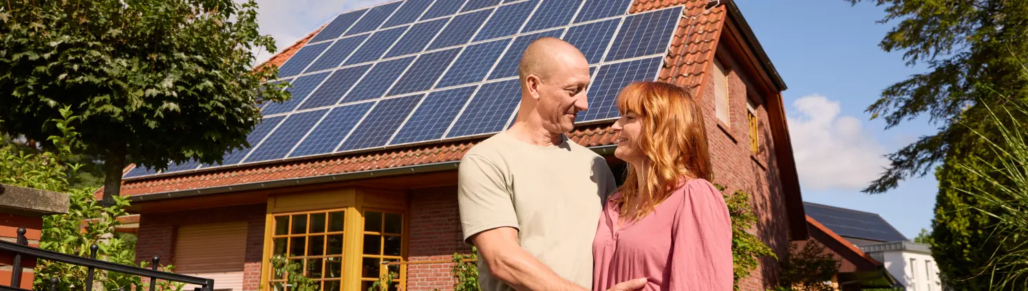 Pärchen steht vor ihrem Haus mit einer PV-Anlage auf dem Dach