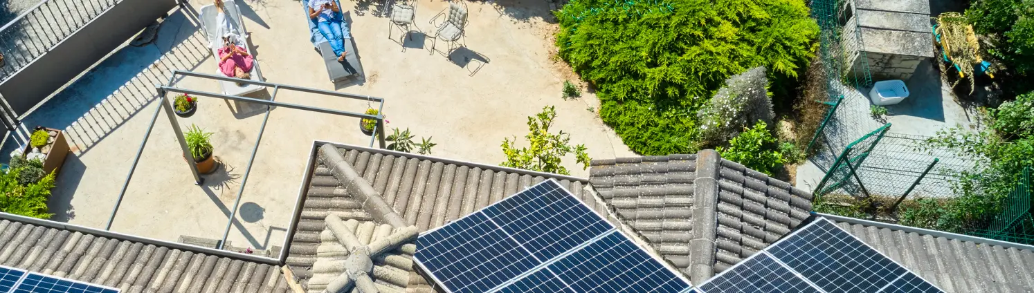 Eine Solaranlage auf einem Haus von oben aufgenommen mit zwei Personen, die auf einer Sonnliege liegen.