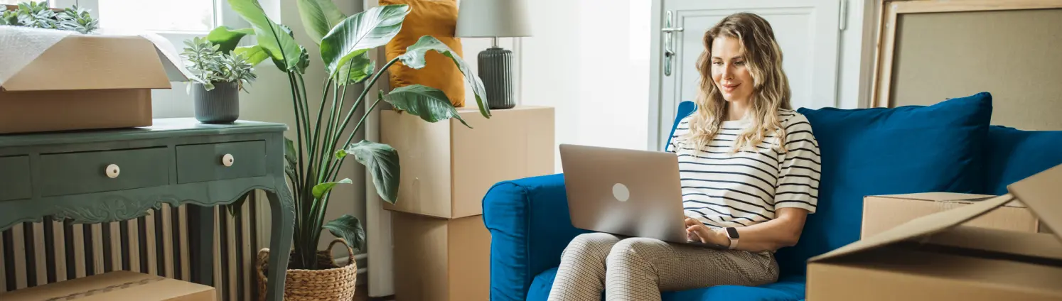 Frau sitzt auf einer blauen Couch und auf ihrem Schoß liegt ihr Laptop, auf dem sie schreibt. Bild mit KI erstellt.