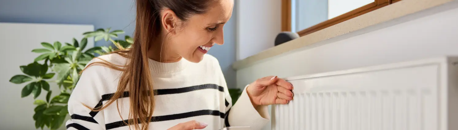Eine Frau sitzt mit ihrem Smartphone vor einer Heizung.