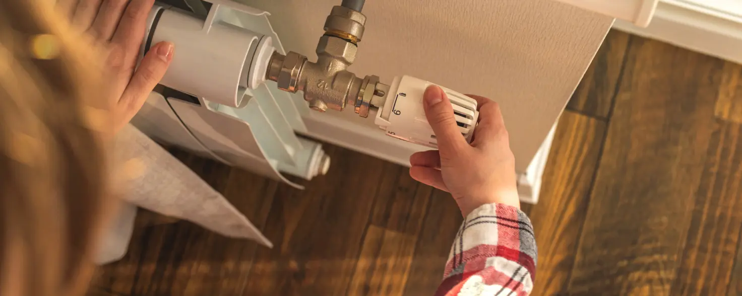 Eine Person regelt die Temperatur einer Heizung. 