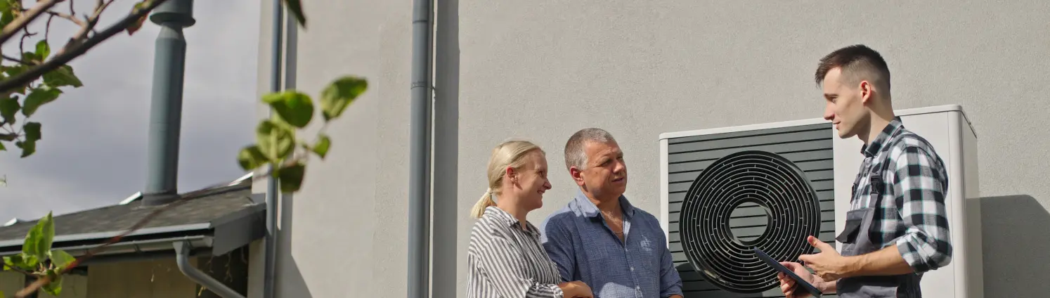Drei Menschen stehen vor einer Wärmepumpe.